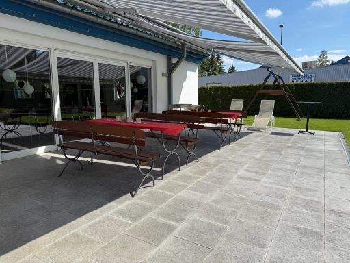Terrasse mit Tisch und Stühlen, neben einem Garten mit Schaukel und Markise.