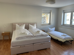 Helles Schlafzimmer mit zwei Betten, Nachttischen und einem zusätzlichen Bett.