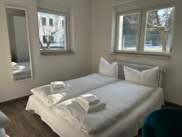 Zimmer mit zwei Betten, weißen Bettwäsche und hellen Wänden, Spiegelfenster sichtbar.