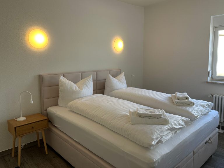 Helles Schlafzimmer mit zwei Betten, Nachttisch und sanfter Beleuchtung.