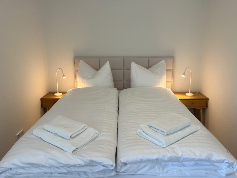 Zwei Einzelbetten mit frischen weißen Bettwäsche und Wäschesets auf nachtblauen Nachttischen.