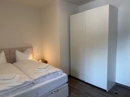 Helles Schlafzimmer mit Doppelbett, weißen Kissen und modernem Kleiderschrank.