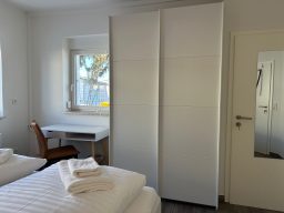 Heller Raum mit zwei Betten, Kleiderschrank, Schreibtisch und Stuhl.