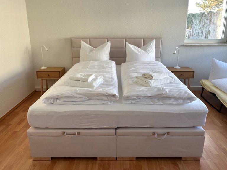 Doppelbett mit weißen Bettwaren und zwei Nachttischen im Hintergrund.