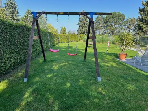 Zwei Schaukeln in einem grünen Garten mit Hecken und Sonnenschein.