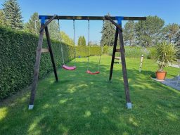 Zwei rote Schaukeln auf einem Holzgestell in einem grünen Garten.