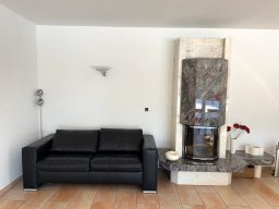 Schwarzes Sofa neben einem modernen Kamin aus Marmor in einem hellen Raum.