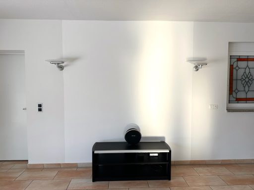 Heller Raum mit Kinowand, schwarzen Sideboard und Wandleuchten an weißen Wänden.