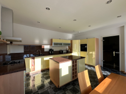 Moderne Küche mit gelben Schränken, Holzdetails und einem Esstisch aus Holz.