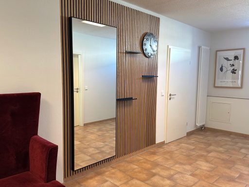 Ein Raum mit einem Rechteckspiegel, Wanduhr und Holzpaneelen. Rote Couch im Vordergrund.