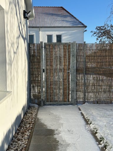 Holztor zwischen einem Zaun und einem Haus, Schnee auf dem Boden.