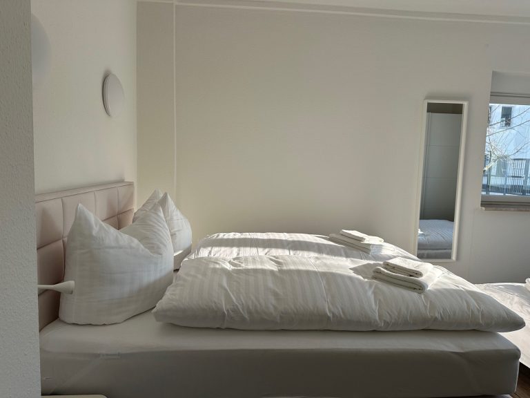 Helles Schlafzimmer mit zwei Betten, jeweils mit Kissen und Bettwäsche, und einem Spiegel.