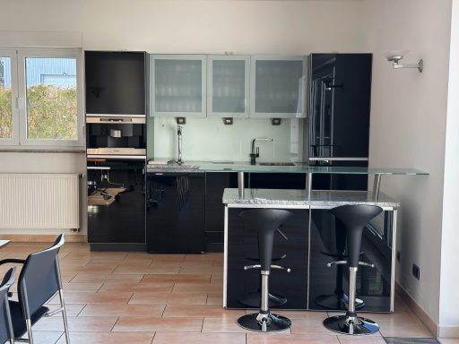 Moderne Küche mit schwarzen Möbeln, Glasoberflächen und Barhockern.