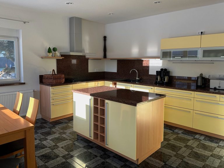 Helle Küche mit gelben Schränken, dunkler Arbeitsplatte und Holztisch.