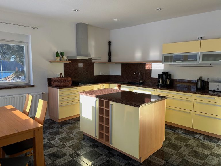 Moderne Küche mit gelben Möbeln, Holzregalen und einem große Kücheninsel.