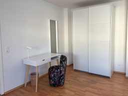 Helle, minimalistische Zimmeransicht mit Schminktisch und großem Schrank.