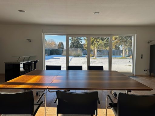 Ein moderner Konferenzraum mit großem Tisch und Fenstern zur Außenansicht.