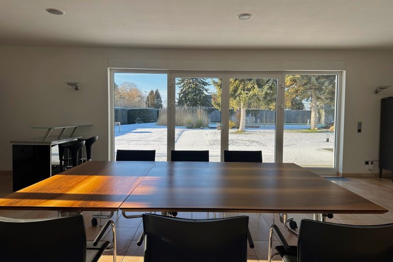 Ein heller Besprechungsraum mit einem großen Tisch und Blick auf einen verschneiten Garten.