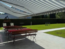 Ein gepflegter Garten mit Liegen, Tischen und Sonnenschutz. Rasenfläche im Hintergrund.