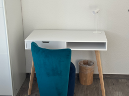 Weißer Schreibtisch mit blauer Stuhl, Papierkorb und Tischlampe.