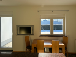 Helle Küche mit Holzstuhlset und Blick auf den Außenbereich durch ein Fenster.