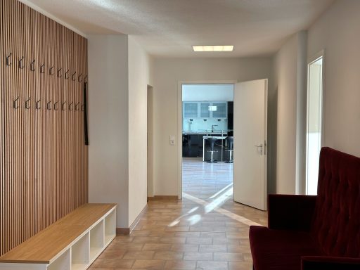Schmaler Flur mit Holzpaneelen, Garderobe und Blick auf einen offenen Wohnbereich.