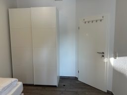 Helles Zimmer mit einem weißen Schrank und einer Tür, darunter ein Bett.